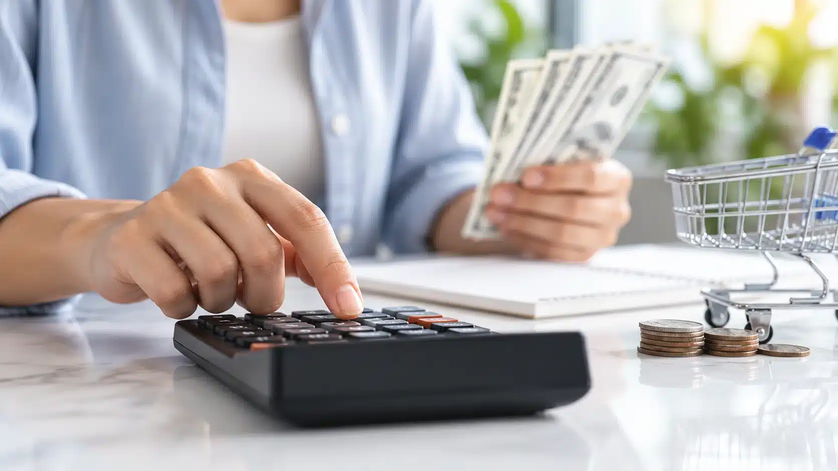 Hand using a calculator while holding cash