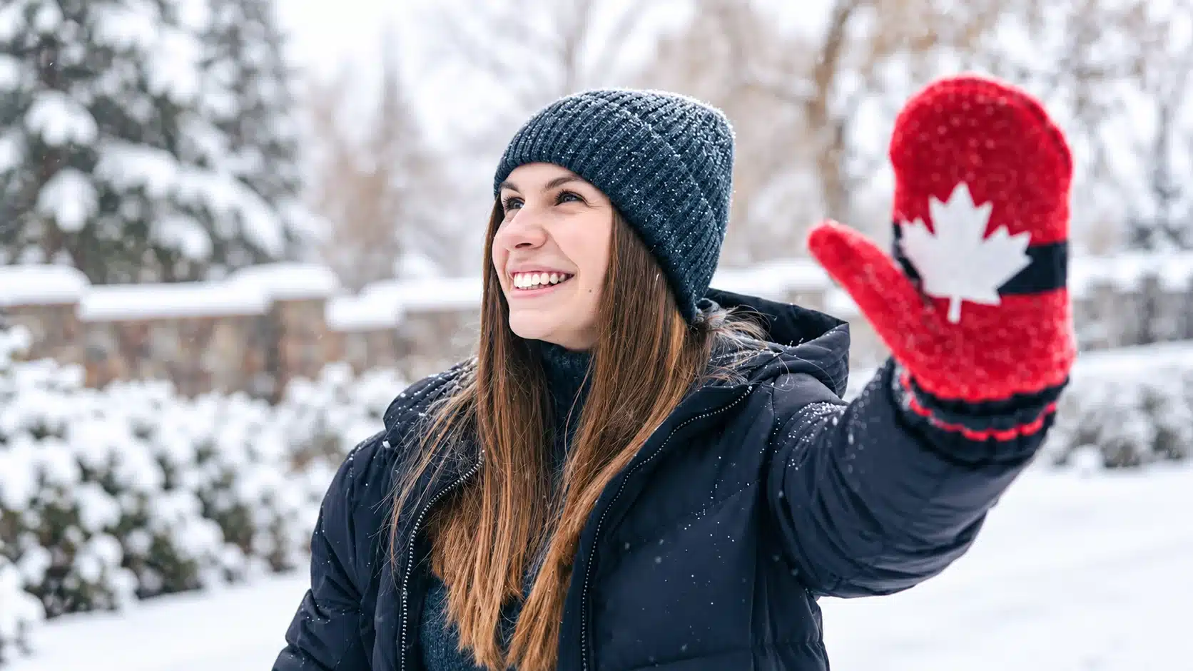 Smiling woman waving a red Canada maple leaf mitten in the snow