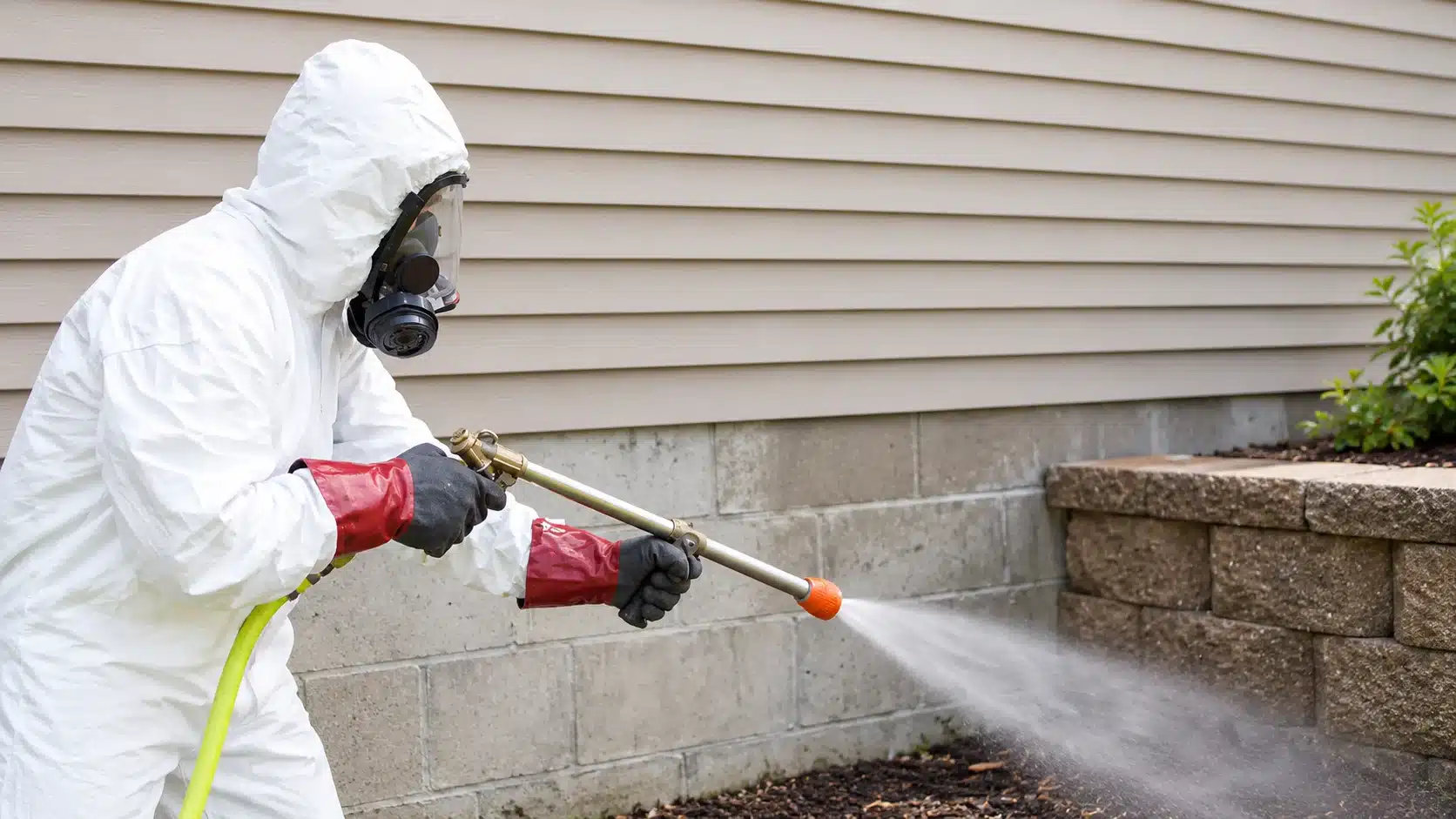 Worker in a protective suit and respirator spraying pesticide