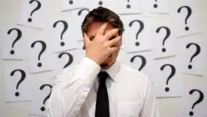 Man with his hand over his face surrounded by question marks