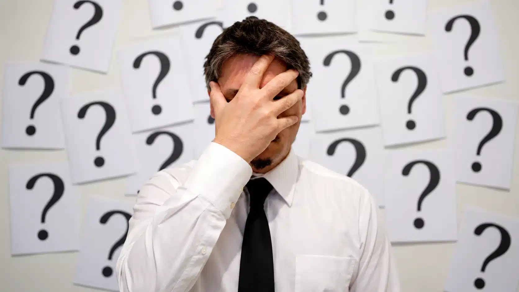 Man with his hand over his face surrounded by question marks